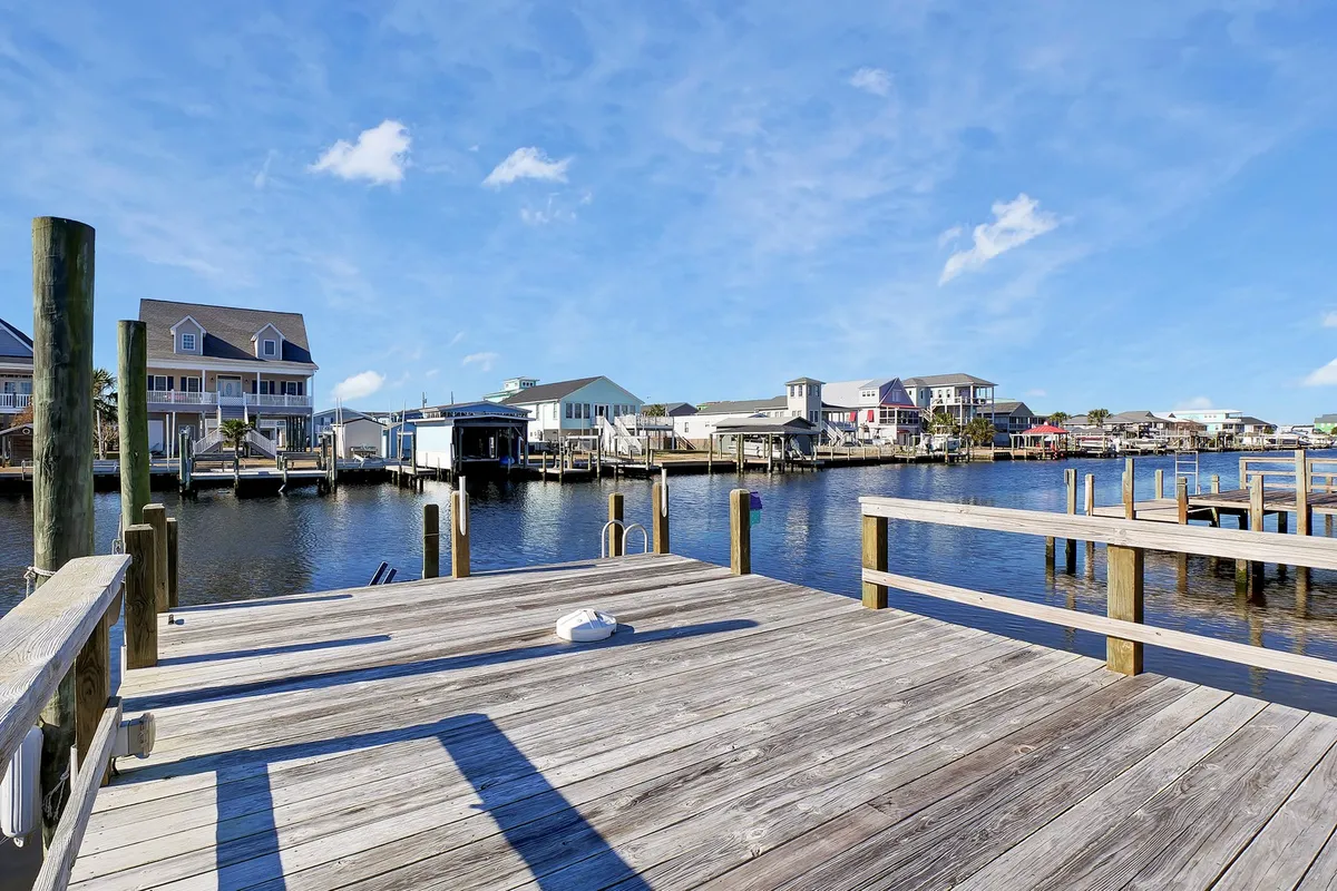A peaceful wooden dock extending over calm waters, framed by surrounding houses. It's a serene spot perfect for fishing, launching a kayak, or simply soaking up sunshine while watching boats on the water.