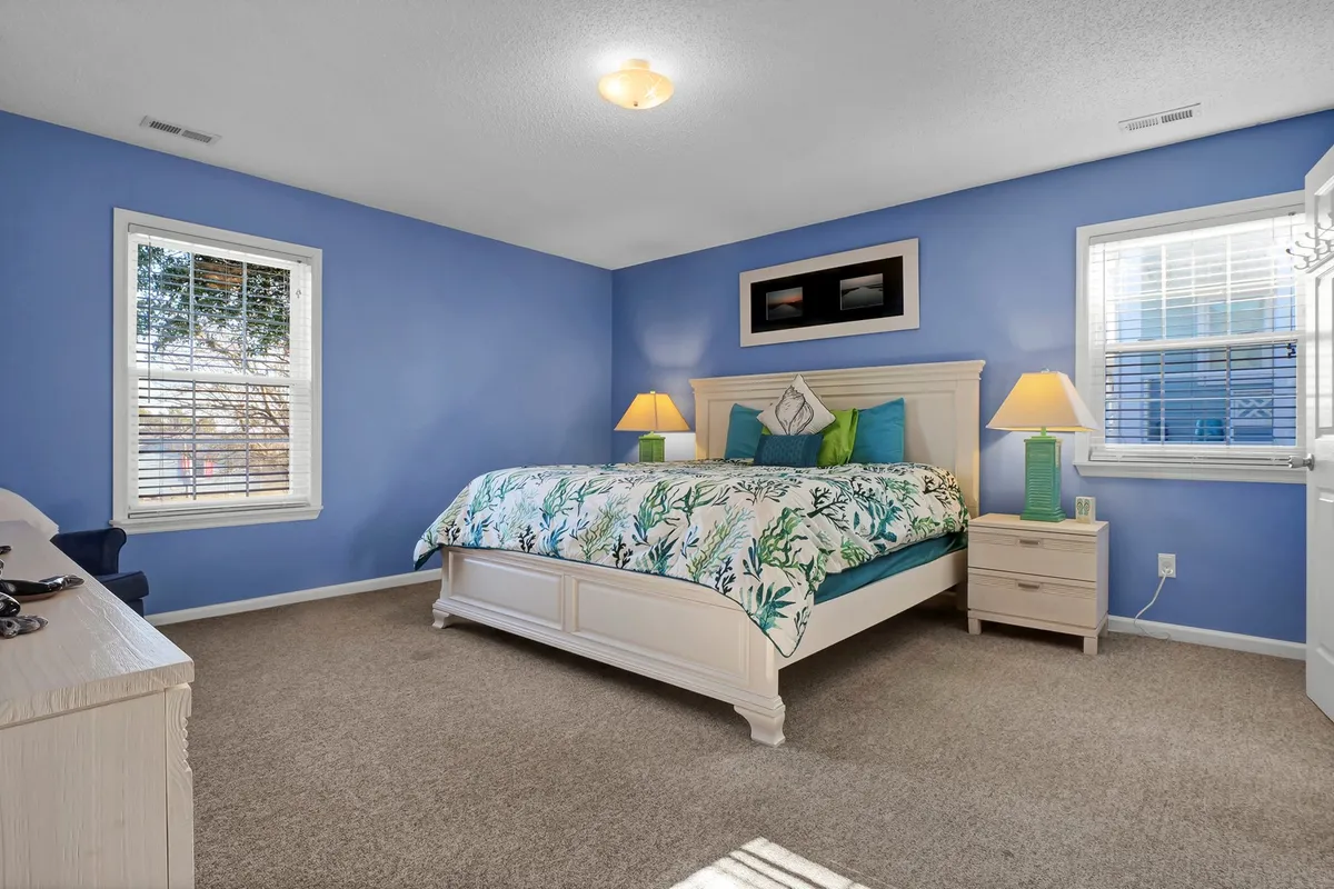 A calming bedroom featuring a bed with a patterned duvet, soothing blue walls, soft lamps, and tasteful artwork. The space feels serene and restful, ideal for relaxing after a full day of activities.