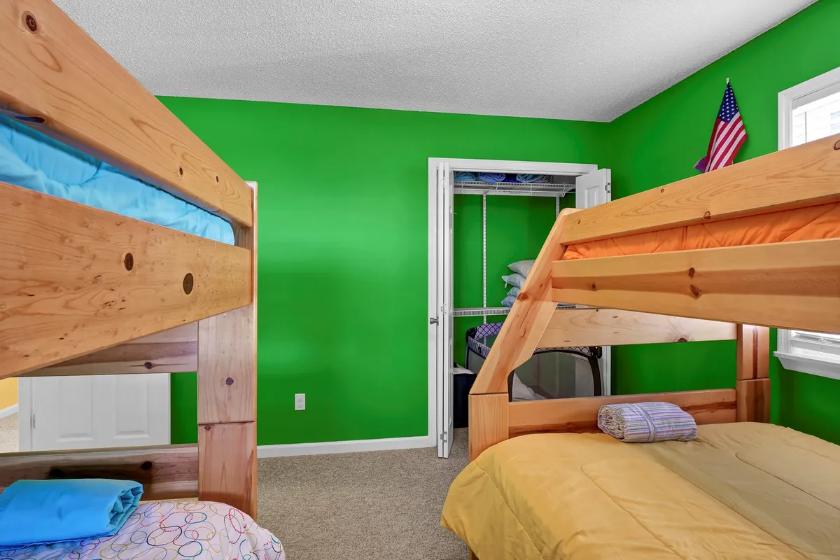 A cheerful bunk room with multiple bunk beds, a bright green accent wall, colorful bedding, and a prominent American flag. The space is energetic and fun, perfectly suited for children or groups of friends.