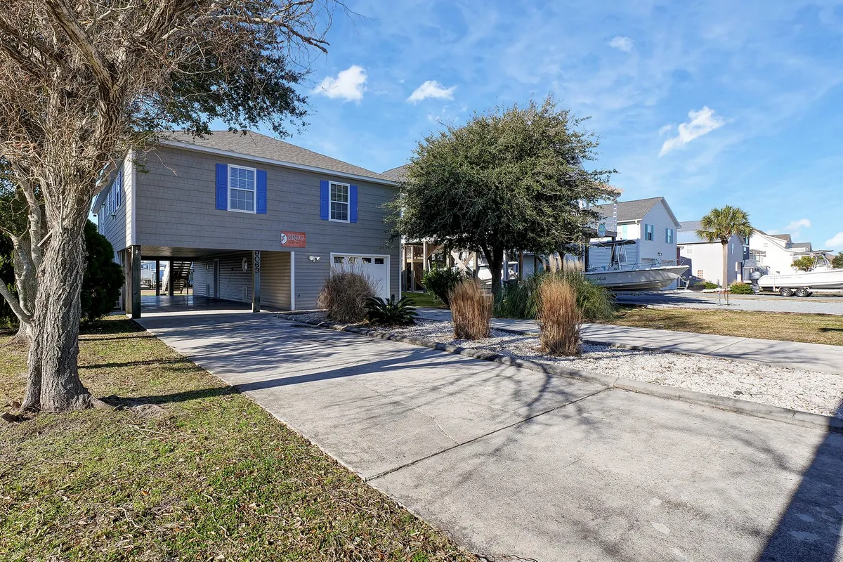This image showcases the house's exterior, including a landscaped yard, driveway, and surrounding trees. The scene is lively and inviting, with areas well-suited for outdoor games, barbecues, and casual gatherings, as suggested by the visible fire pit and open lawn.