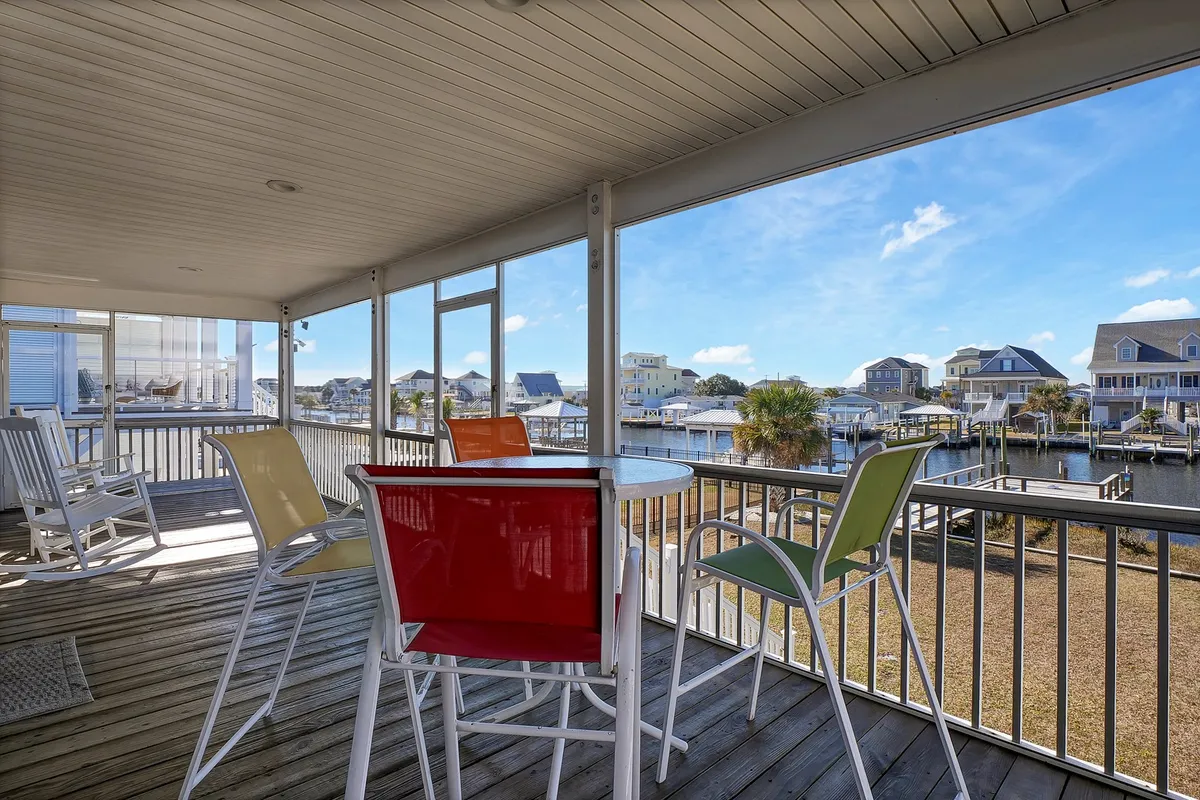 A cheerful setup of colorful chairs and a round table on a porch or deck, positioned to take in a stunning water view. The scene evokes the feeling of a morning coffee or evening meal with the serene backdrop of sunlight glinting on the canal.