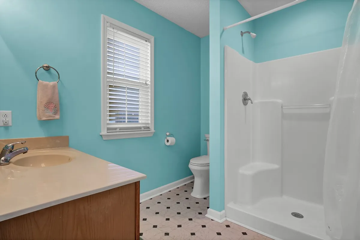 A cheerful bathroom with turquoise walls, a modern vanity and sink, and a glimpse of the shower area. The bathroom feels clean, bright, and inviting, suggesting comfort and convenience for guests.