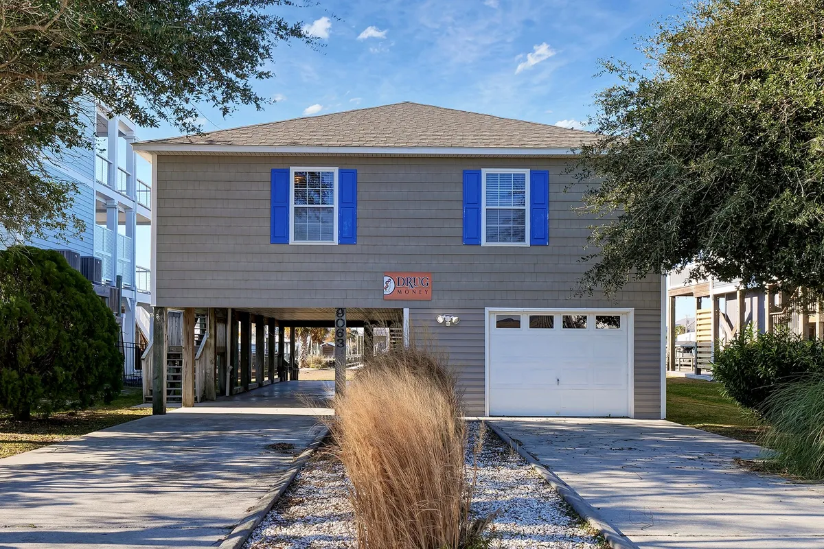 Features the home's exterior with blue shutters, attractive landscaping, and welcoming signage. The porch and driveway are focal points where families or friends might gather for morning coffee or evening games.