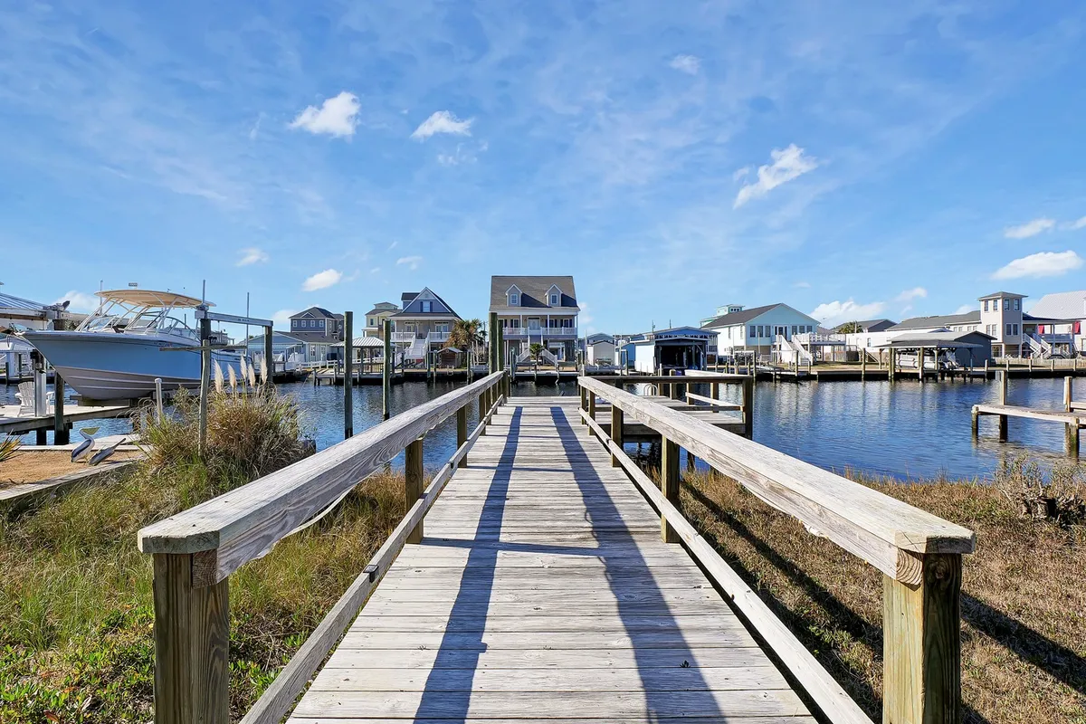 This image captures a wooden dock extending over the canal, with boats moored nearby and waterfront houses lining the opposite shore. The scene radiates calm, with gentle ripples on the water and soft, golden sunset lighting. The dock and boats are central, inviting viewers to imagine stepping right onto the water for kayaking, fishing, or boating adventures.